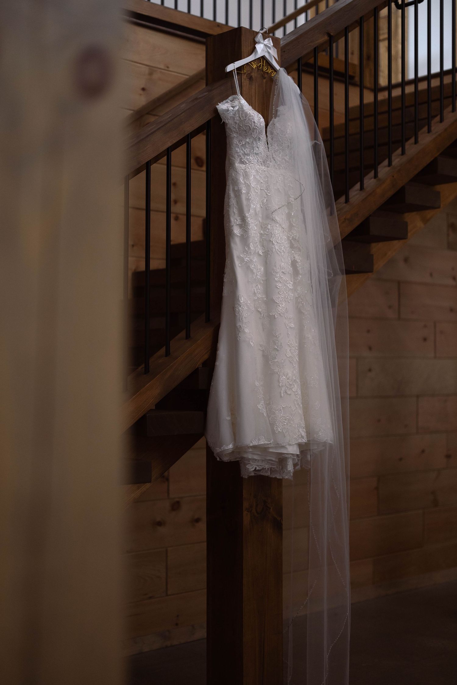 White lace wedding dress and veil hanging elegantly against wooden stairs and railing.