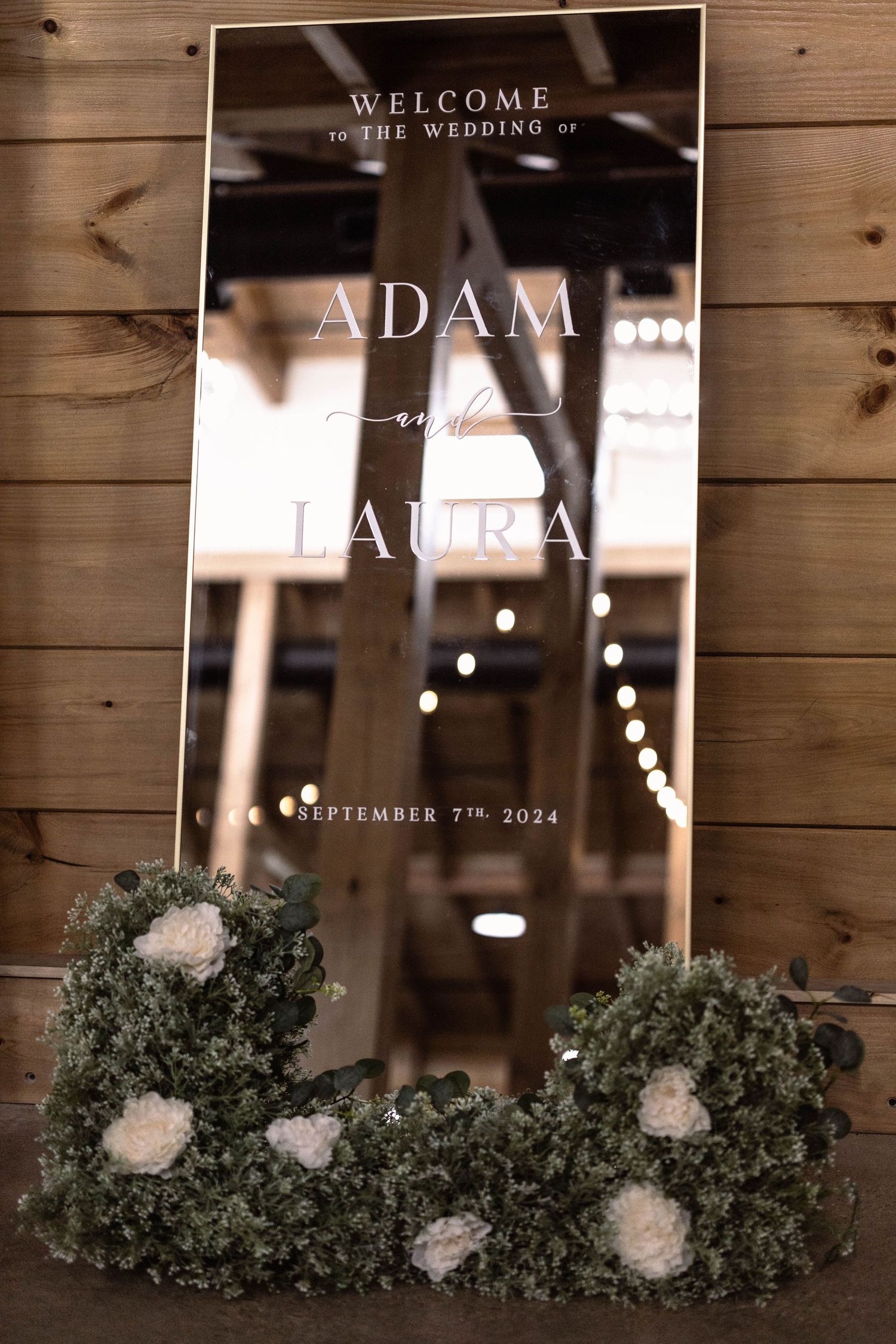 Rustic wooden wall decor displays welcome sign and wedding date for Adam and Laura's September 2024 celebration.