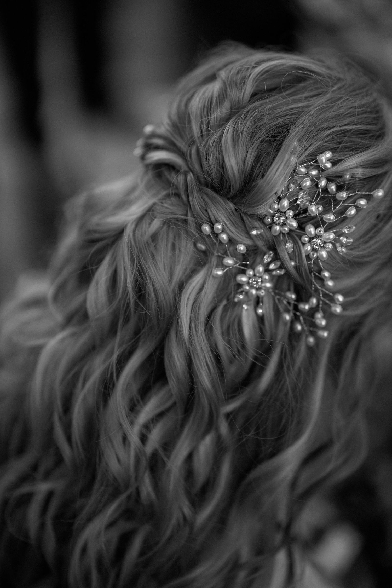 A detailed black and white photo of an elegant bridal hairstyle with delicate pearl hair accessories.