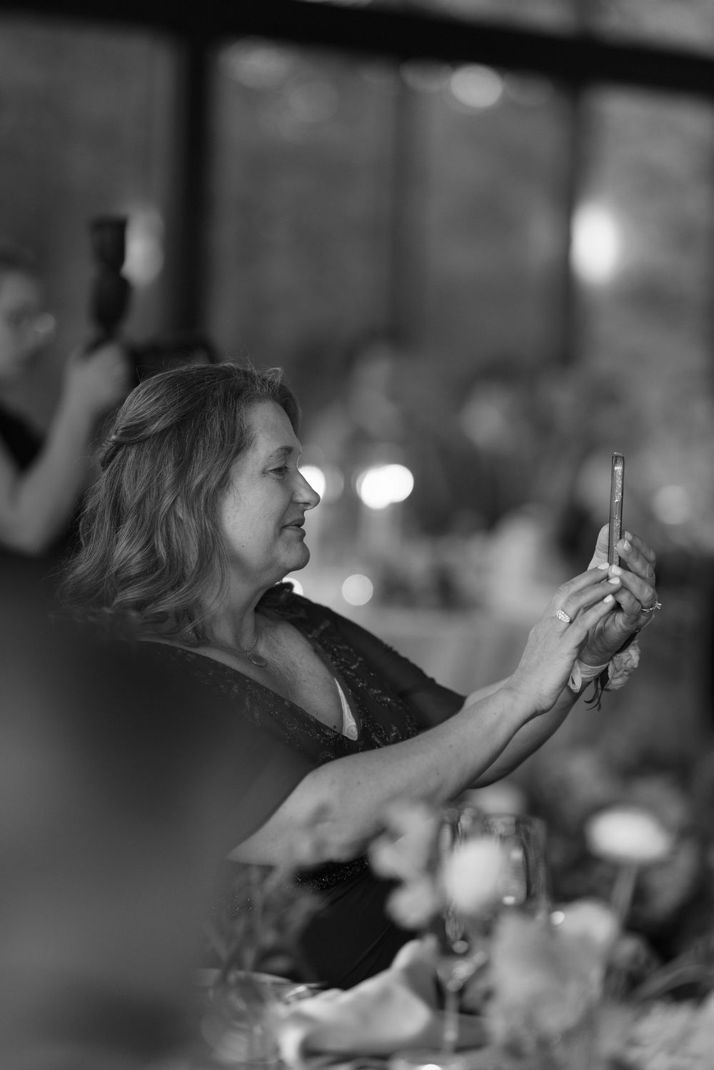 Side profile view of someone taking photos with their phone at an indoor event with blurred bokeh background lighting.