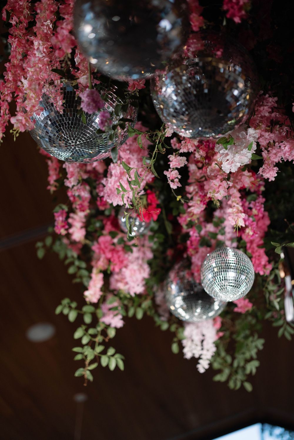 Disco balls and pink floral decorations create a romantic ambiance with hanging cherry blossoms and greenery.
