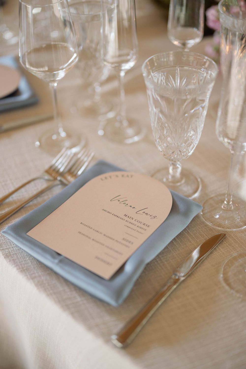 Elegant place setting with crystal glassware and menu card on light blue napkin at formal event.