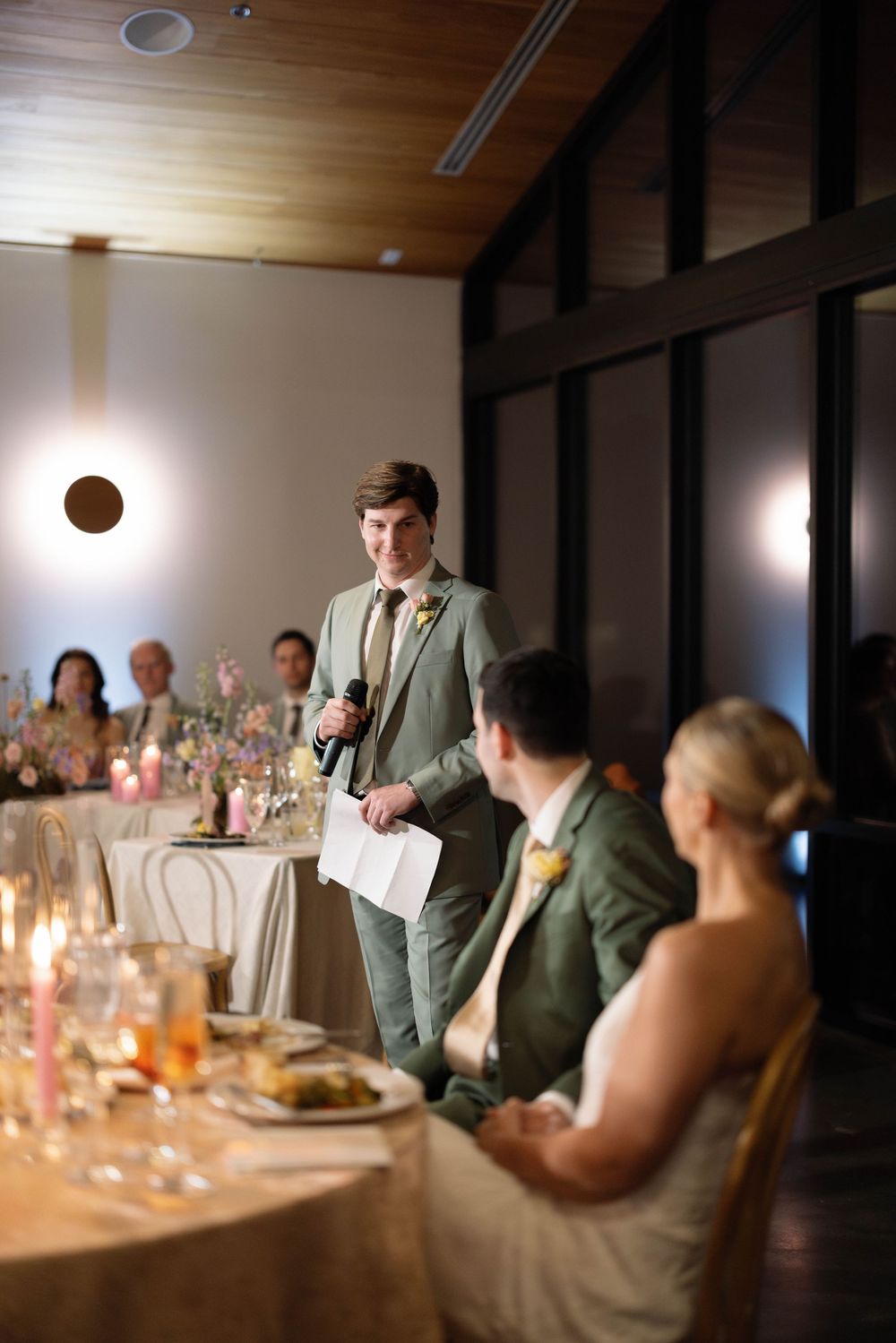 Wedding reception dinner guests seated at elegant tables with romantic candlelight and soft ambient lighting.