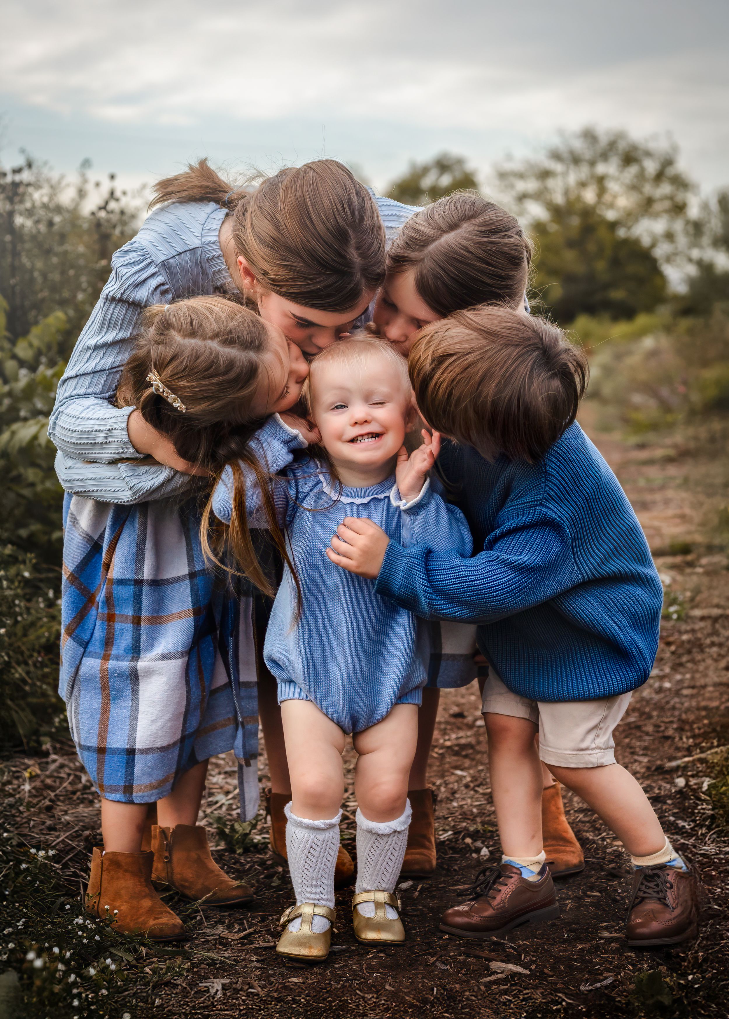 Four big siblings, dressed in blue kiss their baby sister in a field, captured by Charlottesville family and newborn photographer.