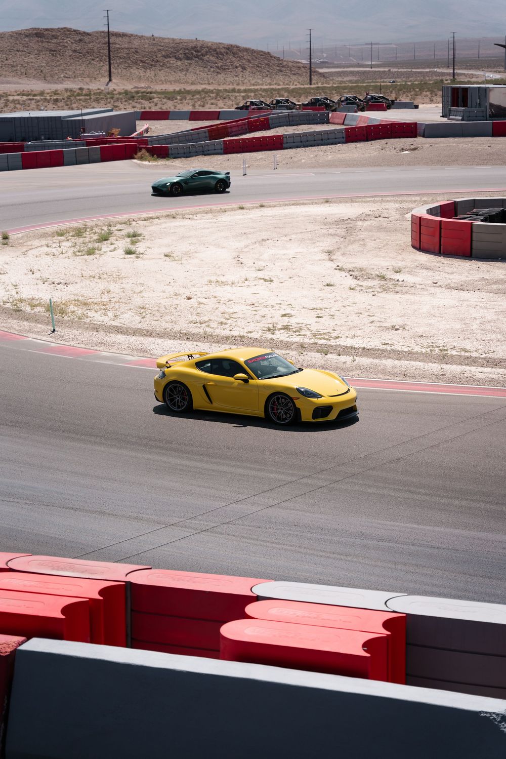 A bright yellow Porsche sports car races around a desert racetrack with red and white barriers.