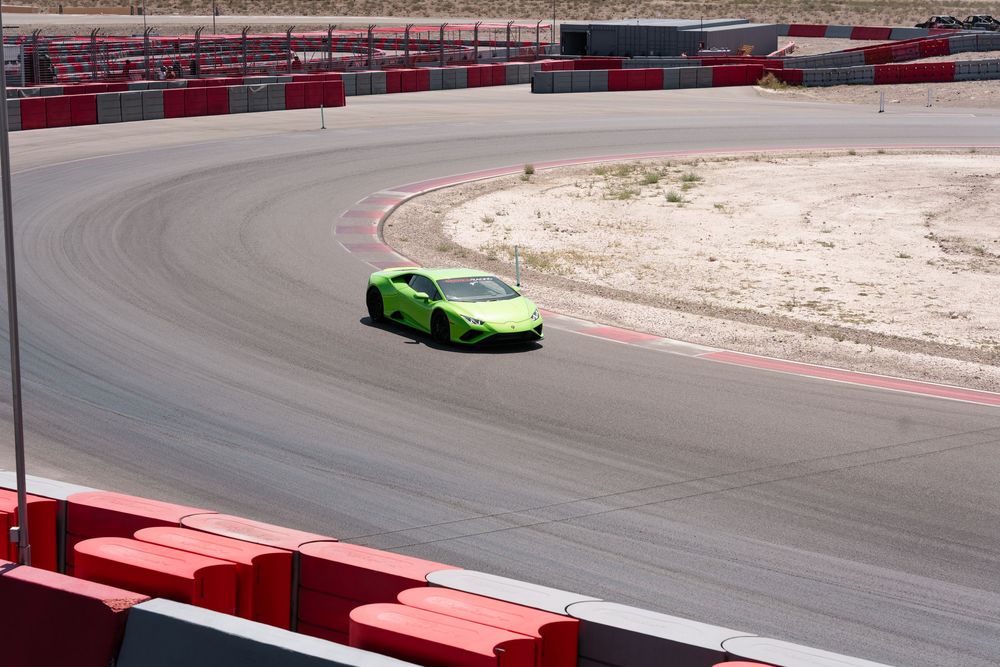 Bright green Lamborghini sports car racing around a curved racetrack with red and white barriers.
