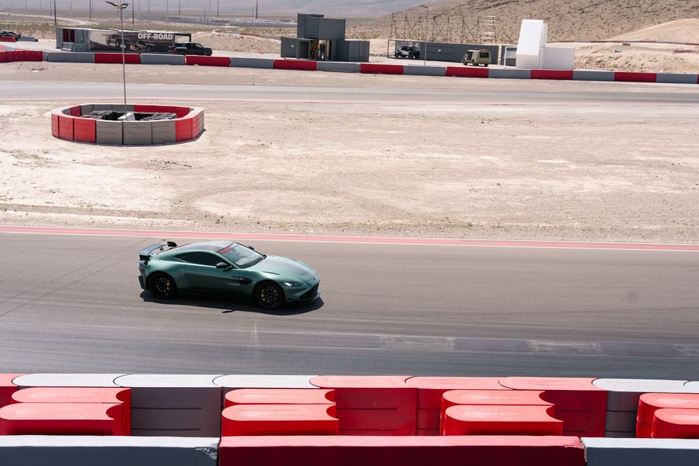 Sports cars race around a desert track with red and white curbing visible on the circuit edges.