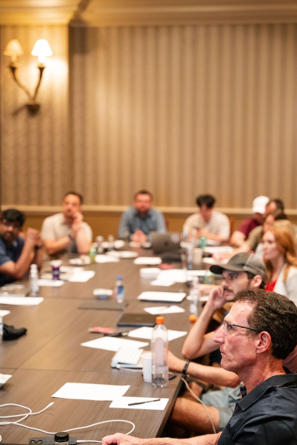 People seated at conference tables in a hotel meeting room with warm lighting and papers in front of them.