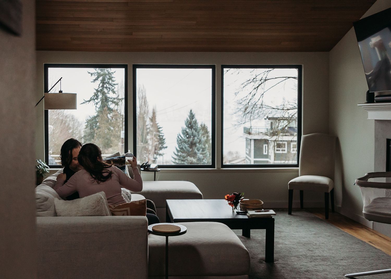 Cozy living room with large windows overlooking snowy winter trees and a modern coffee table setup.