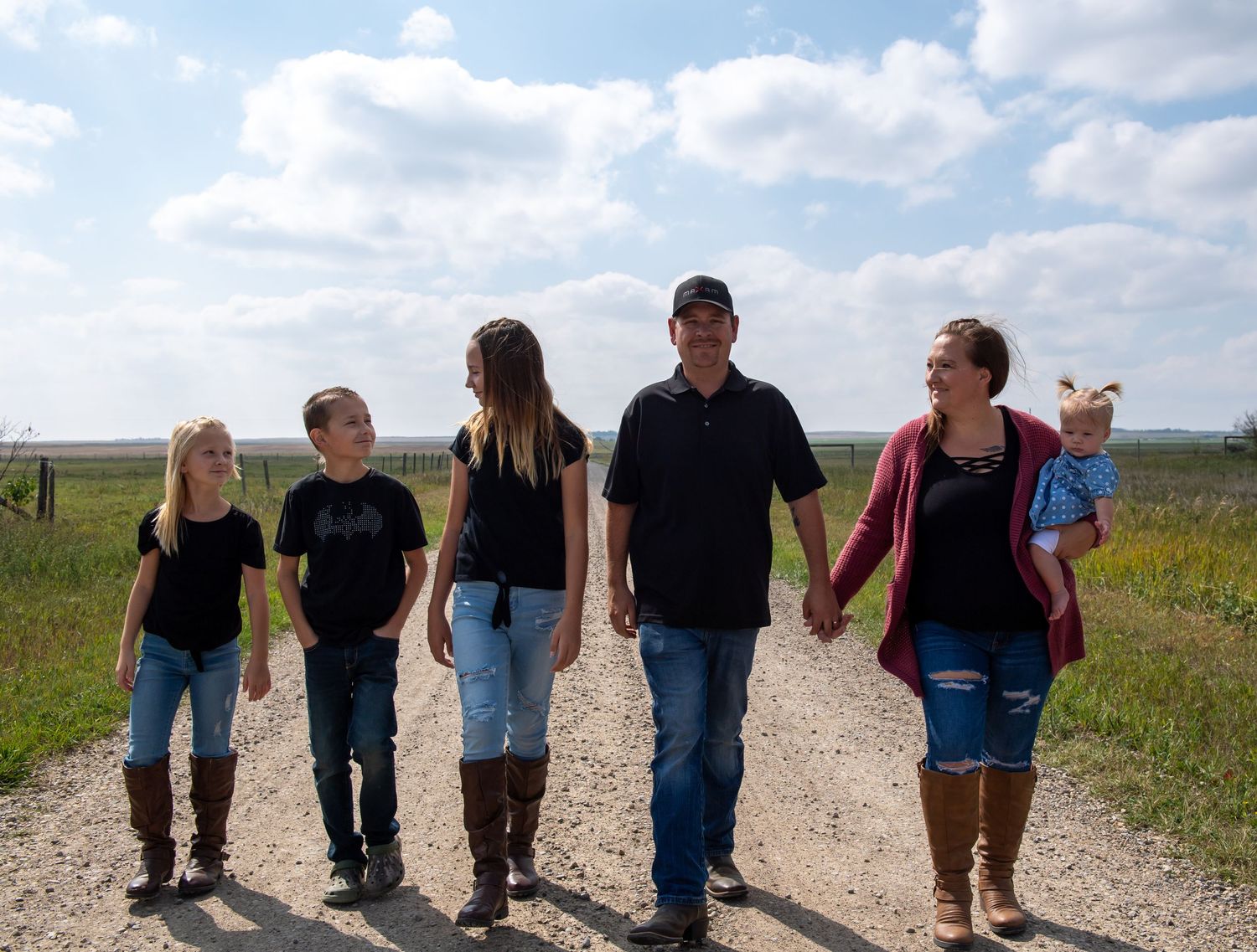 A group of people walking hand in hand down a gravel path through a rural countryside on a sunny day.