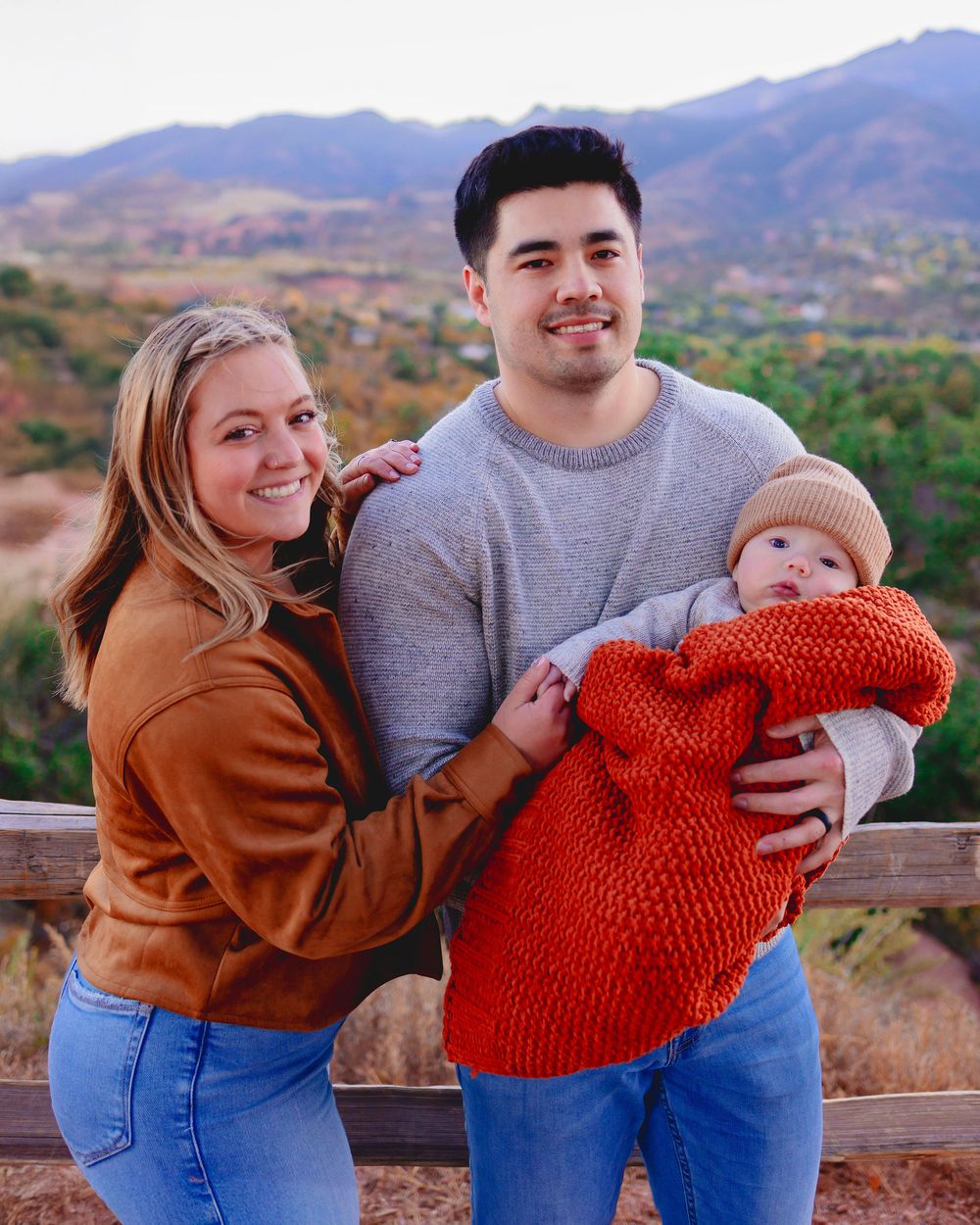 A family poses together on a scenic overlook during autumn with mountains and colorful foliage in the background.