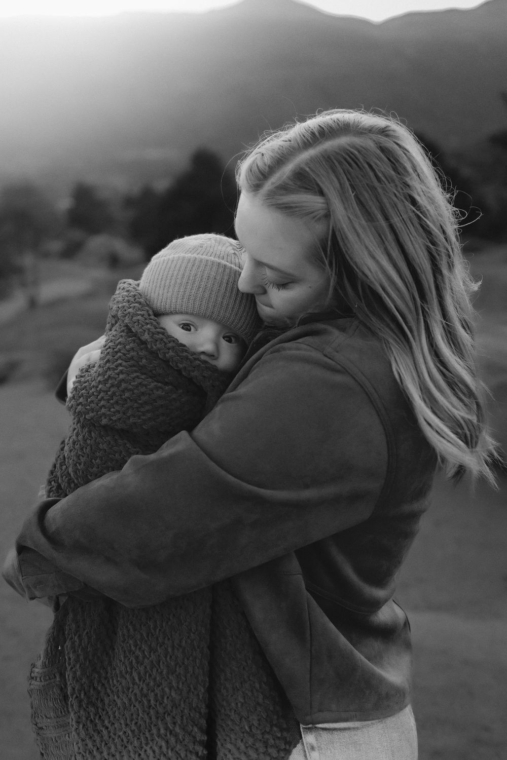 A tender embrace between mother and baby is captured in black and white against a mountainous backdrop.