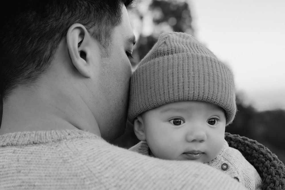 A black and white photograph showing tender moment between father and baby boy in close-up portrait.