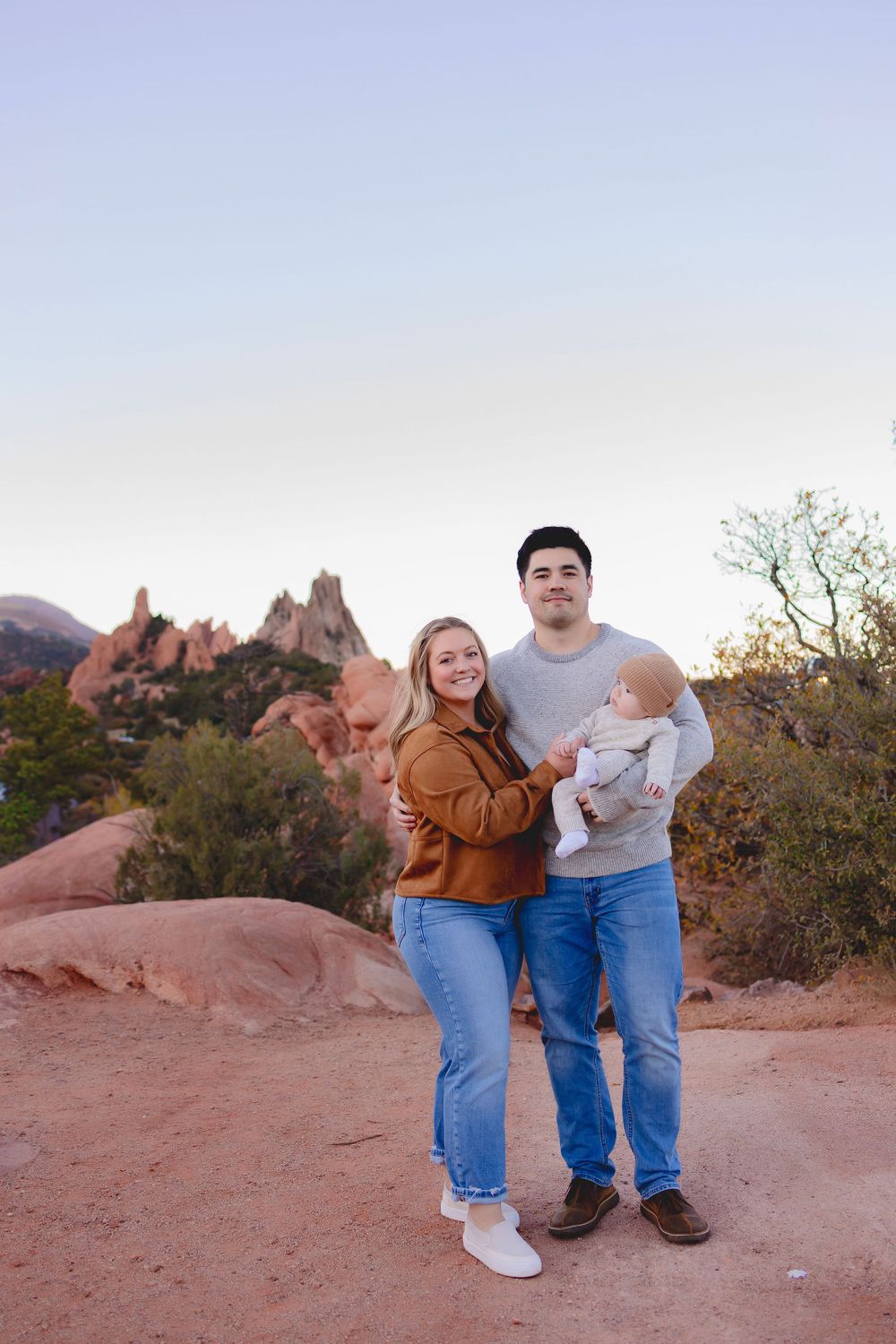 A family stands together on red rocks at Garden of the Gods park in Colorado during sunset.  Mom, Dad and baby boy