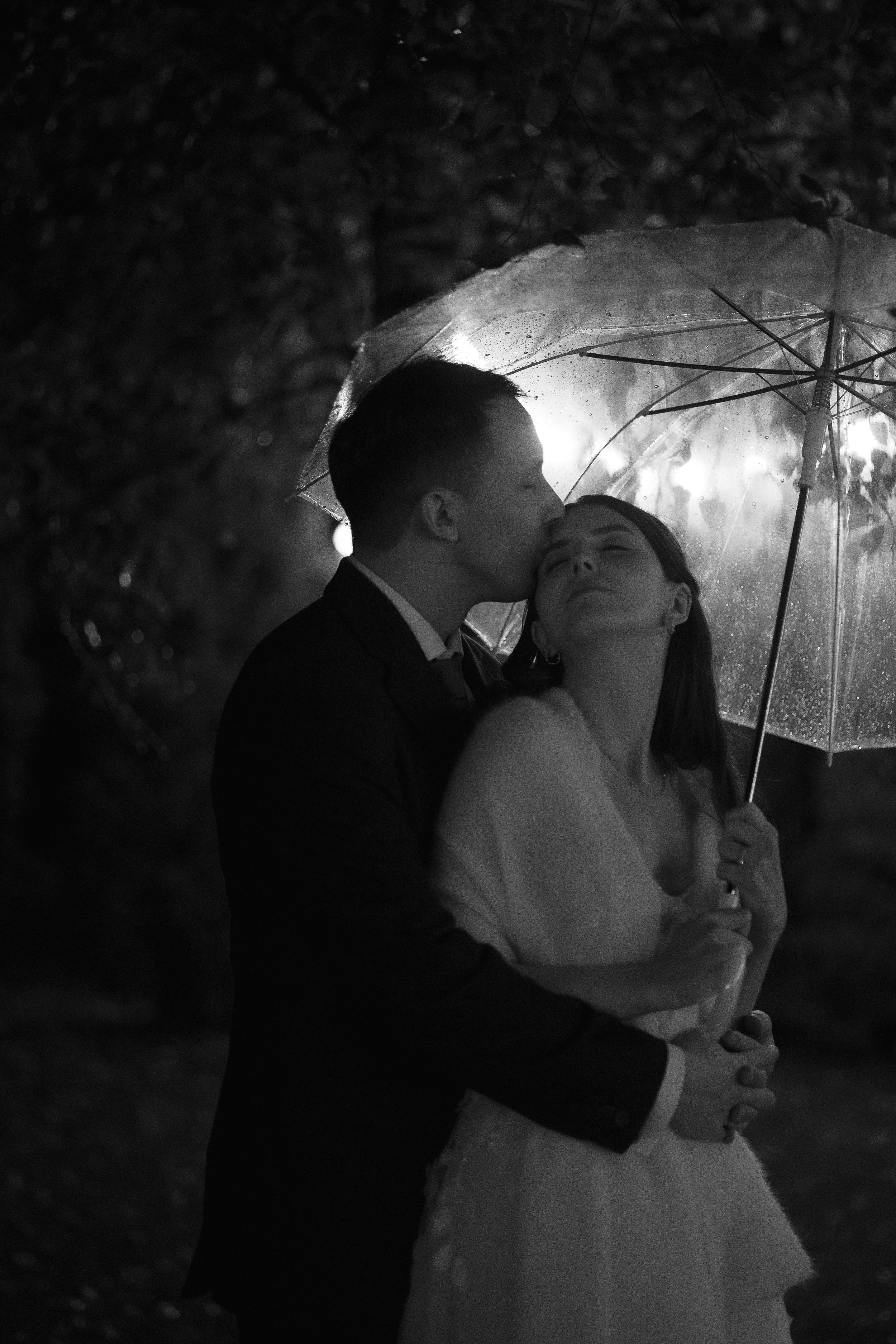 Romantic couple shares intimate moments under an umbrella at night in a series of black and white photographs.
