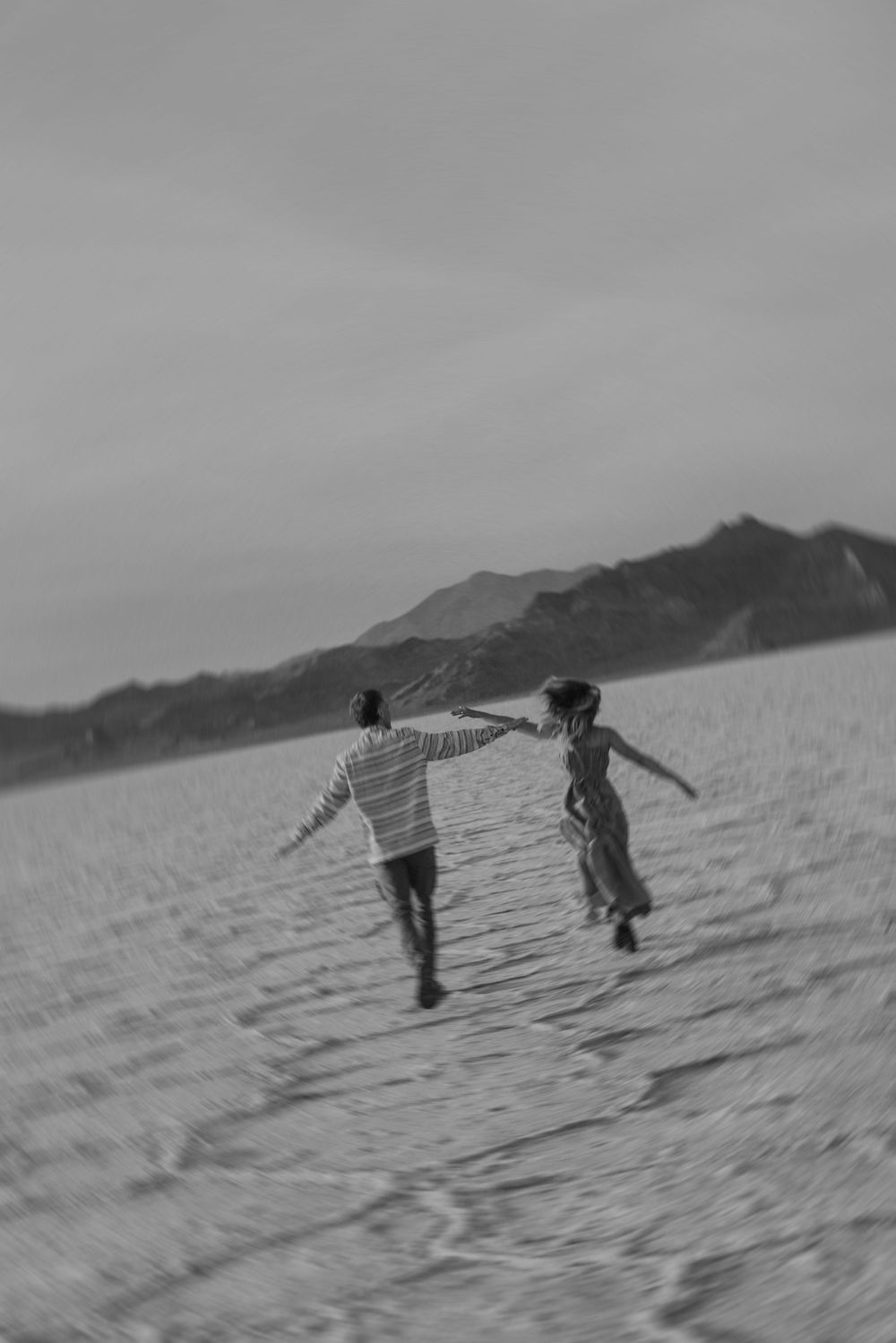 Children run and play on a sloping sand dune against a cloudy sky in this black and white photograph.