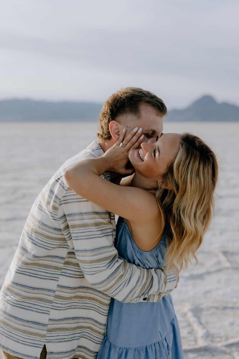 A couple shares intimate moments in a series of romantic photos against a bright white salt flat landscape and mountain backdrop.