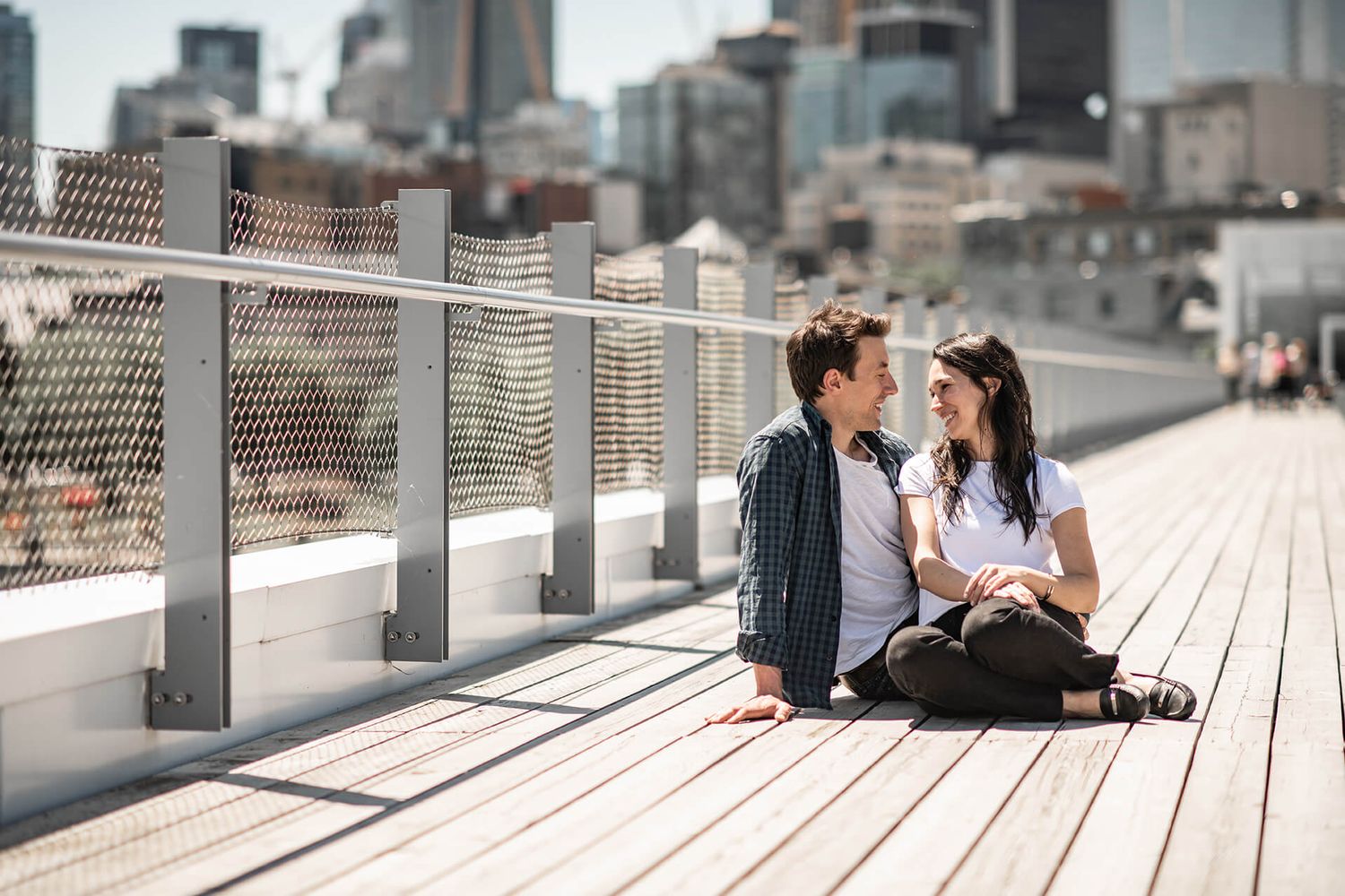 Romantic couple sitting on modern wooden deck with urban skyline backdrop.