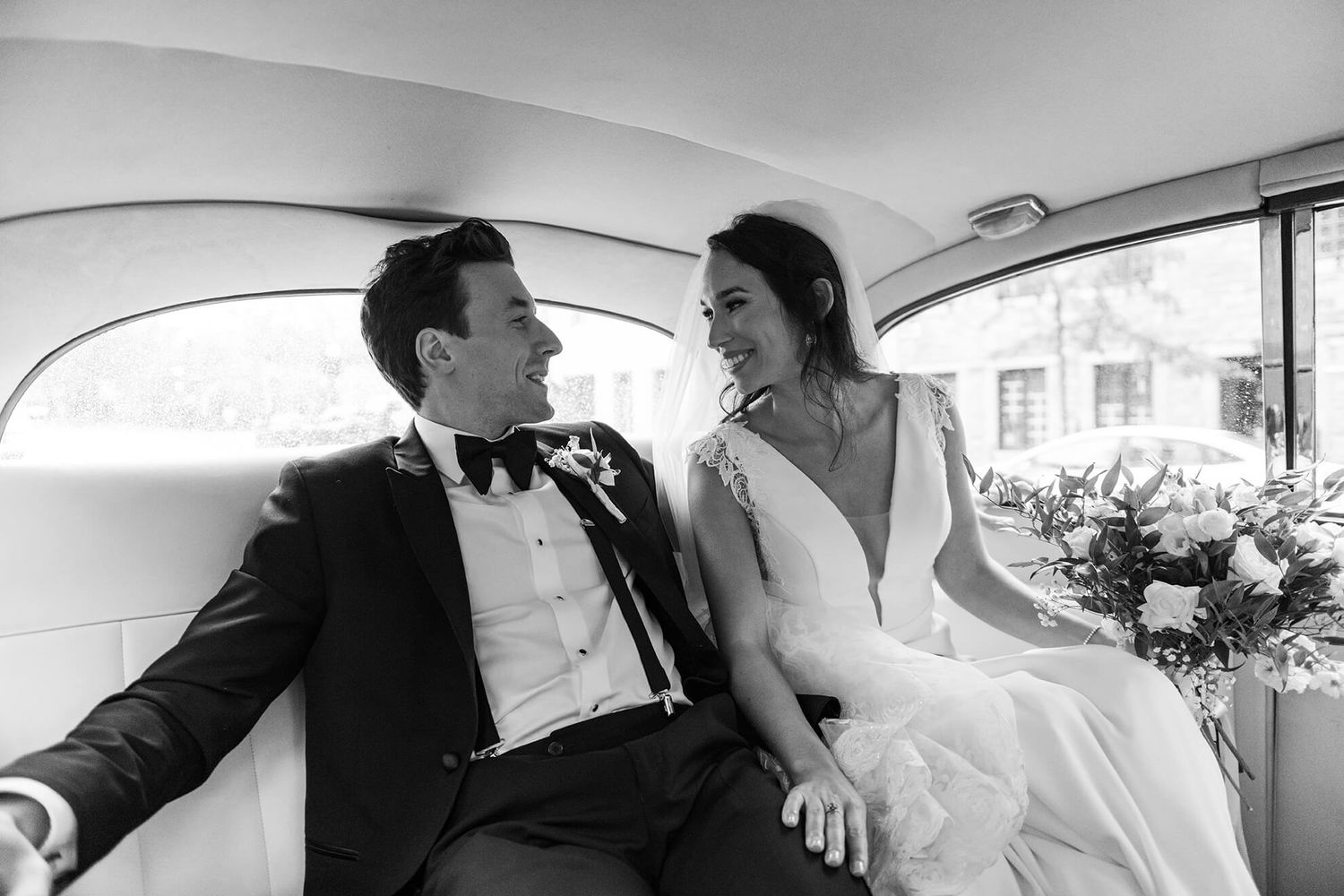 Black and white photo of couple sharing romantic moment in classic car interior.