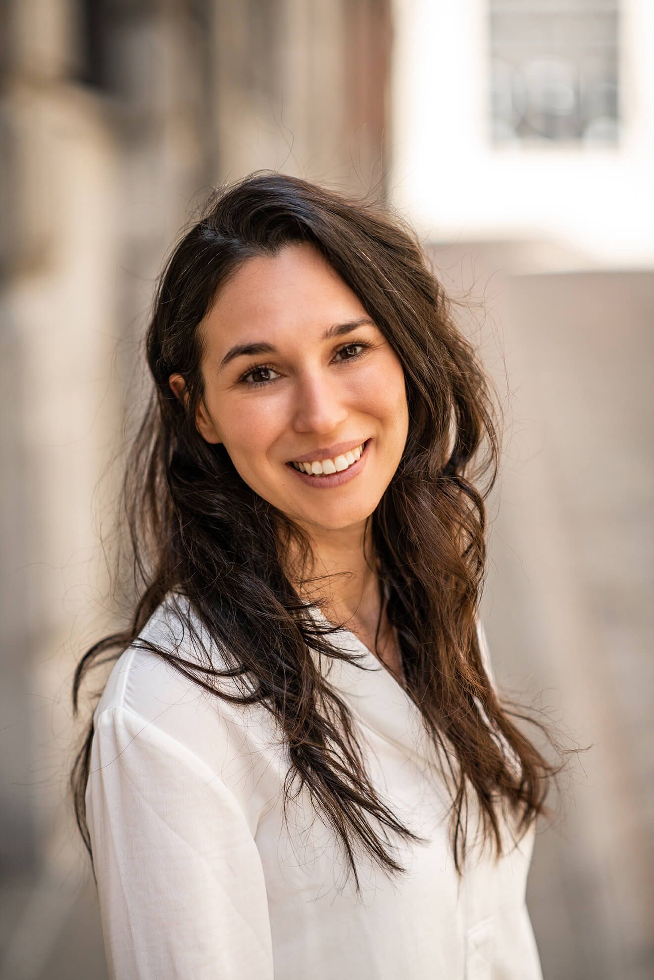 Woman in white shirt smiling with windswept hair in natural light portrait series.
