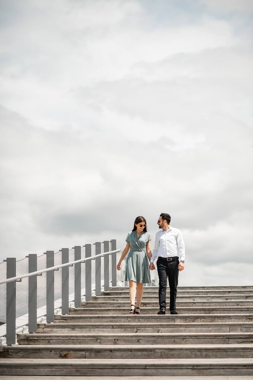Couple walking up concrete steps against cloudy sky in minimalist architectural setting.