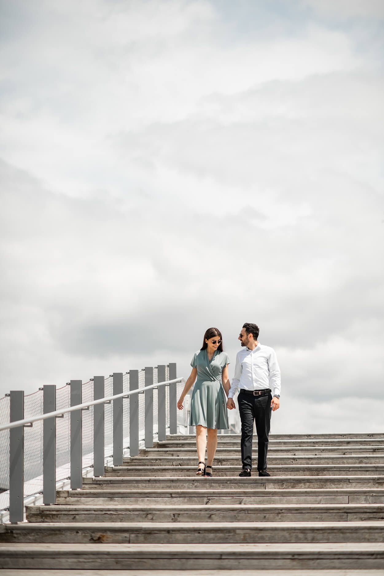 Couple walking up concrete steps against cloudy sky in minimalist architectural setting.