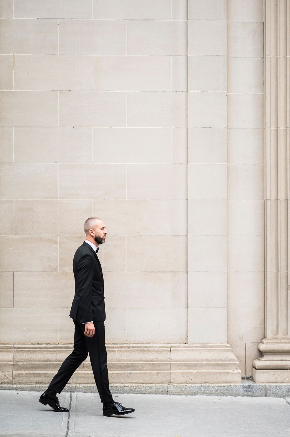 Man in formal attire walking past elegant stone wall with architectural details.