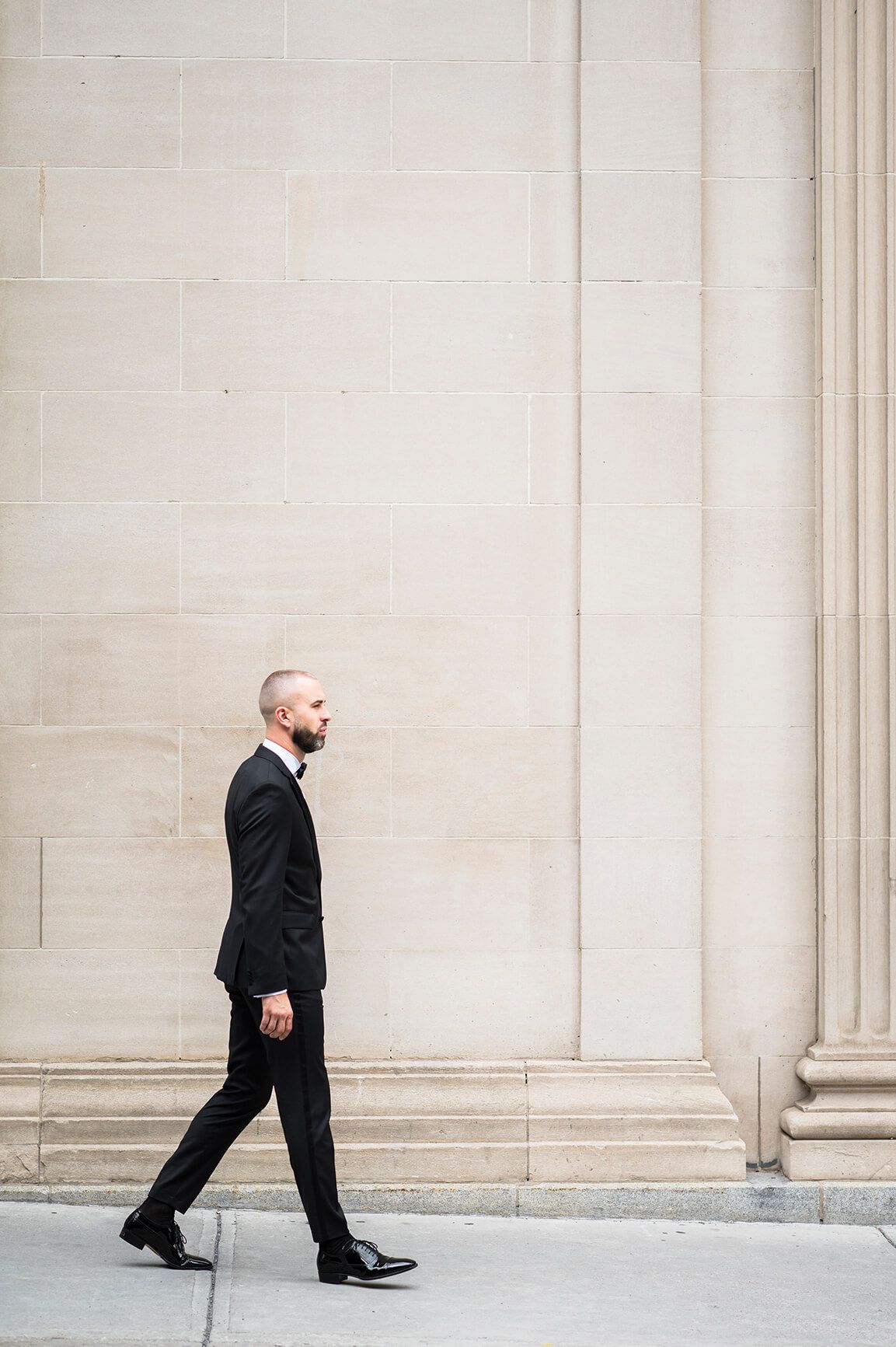 Man in formal attire walking past elegant stone wall with architectural details.