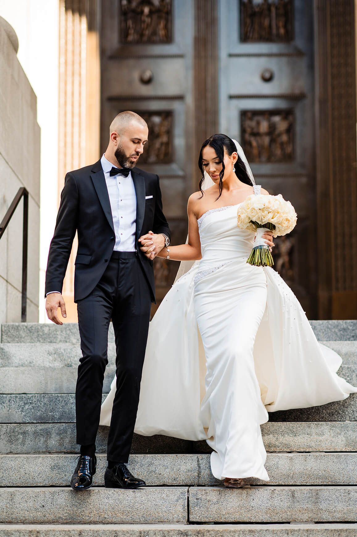 Wedding couple shares joyful moment on grand stone steps of historic building.