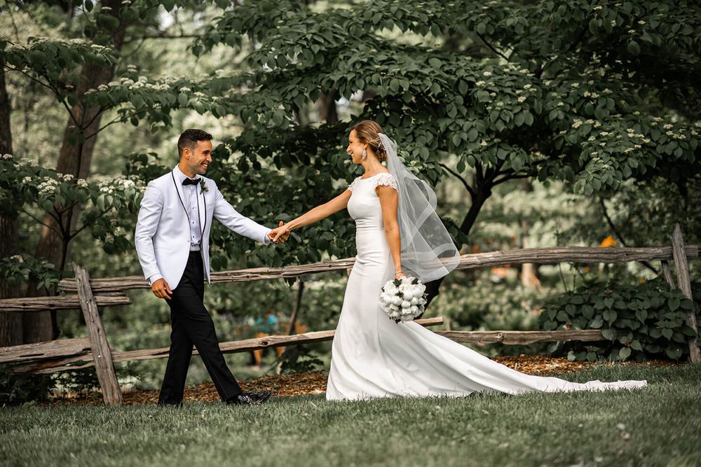 A couple walks hand in hand through a lush garden pathway during their wedding photoshoot.