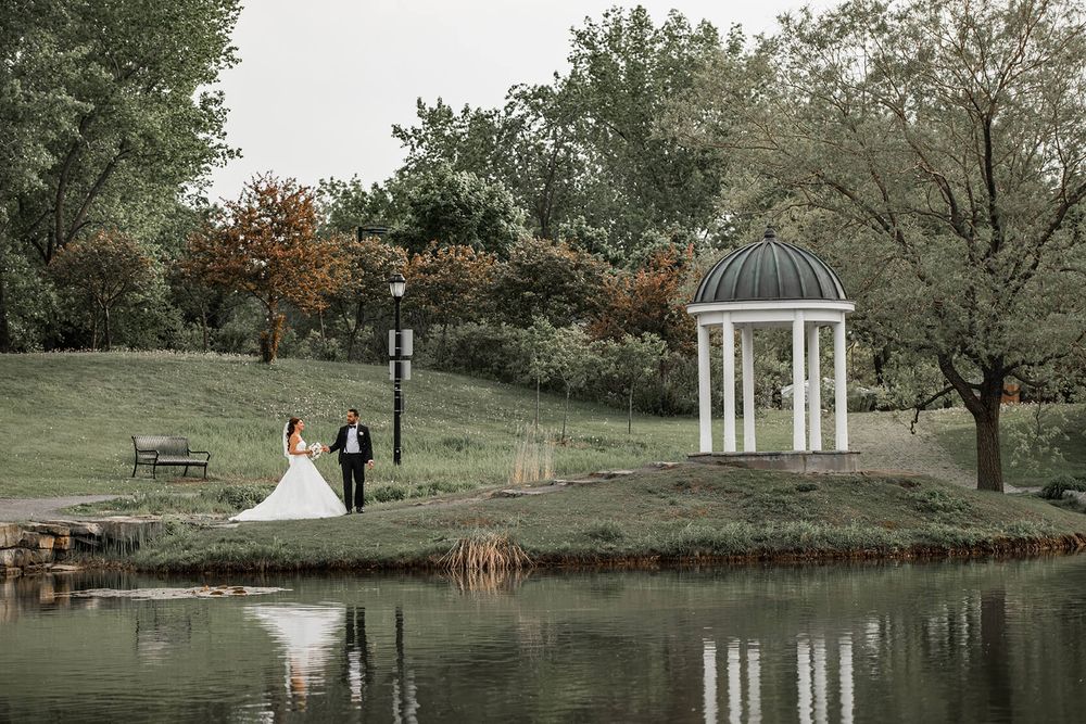 Panoramic view of a wedding venue with gazebo and pond in a serene park setting.
