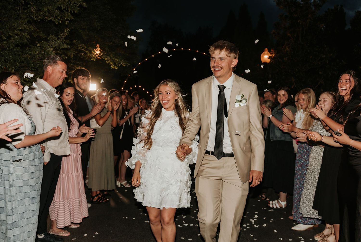 Le Jardin Joyful wedding exit through sparkler tunnel with guests in evening celebration.