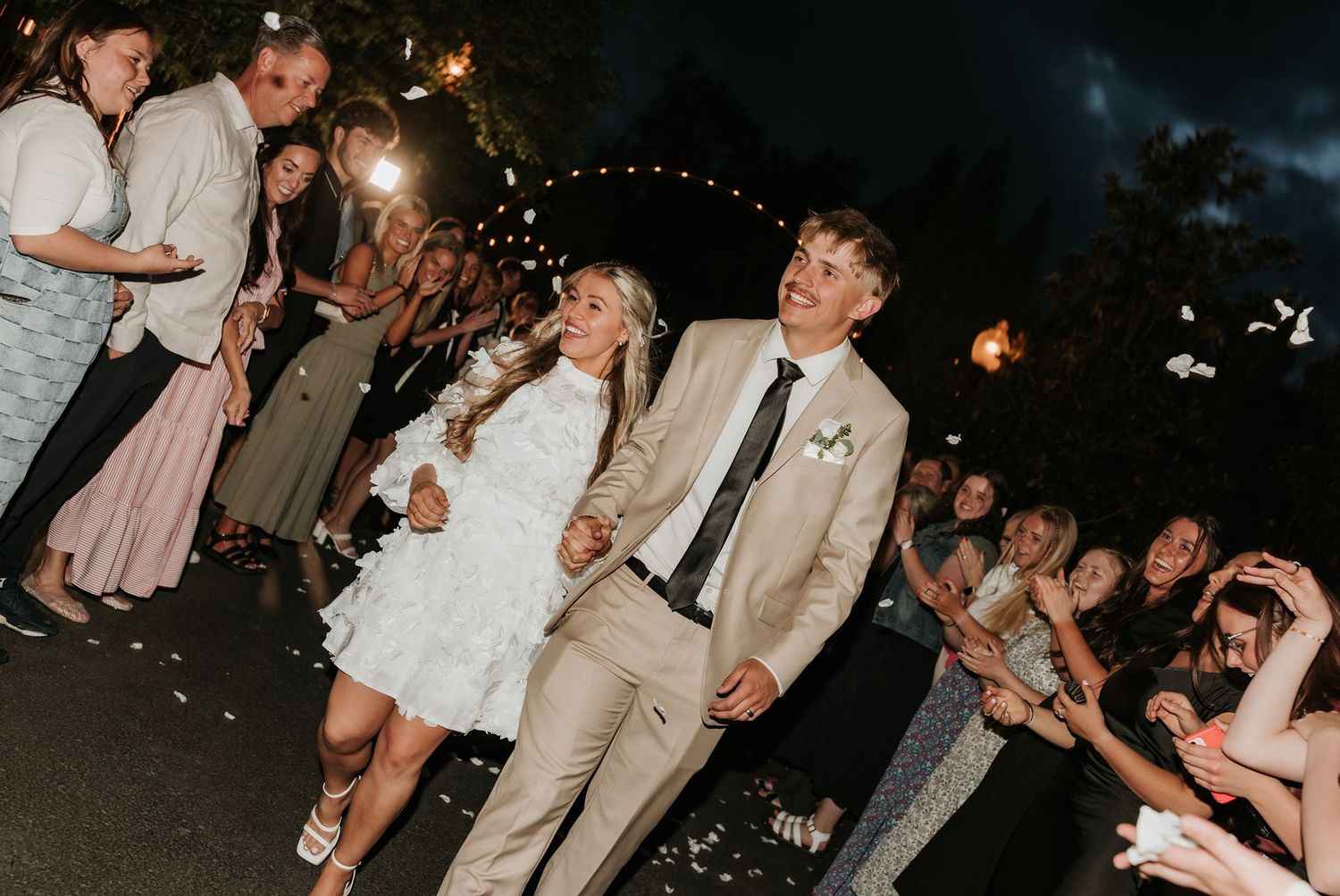 Wedding couple exits their reception at night through a sparkler tunnel lined with guests.