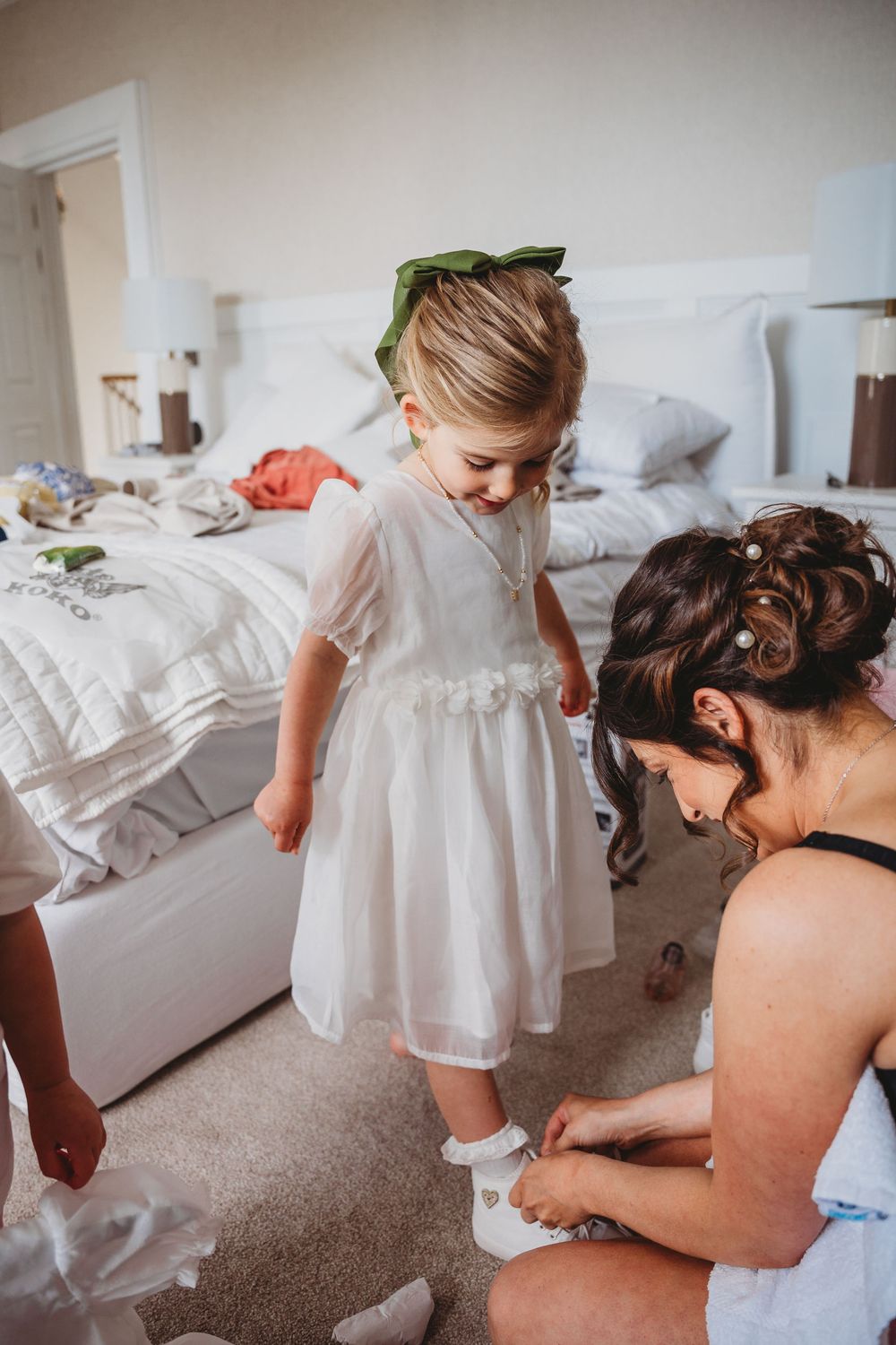 Intimate getting ready moments show a white christening dress being fitted on a small child.