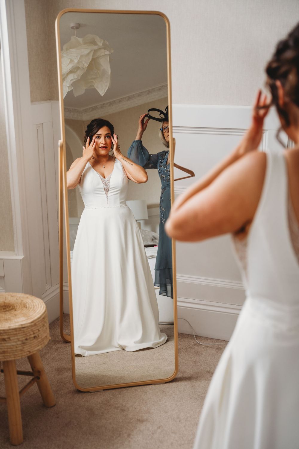 Bride looking at wedding dress reflection in wooden framed mirror.