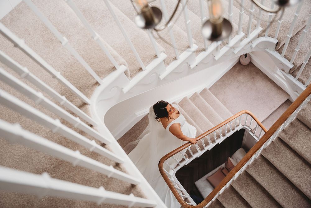 A bride in a white dress descends an elegant spiral staircase in dramatic overhead shot.