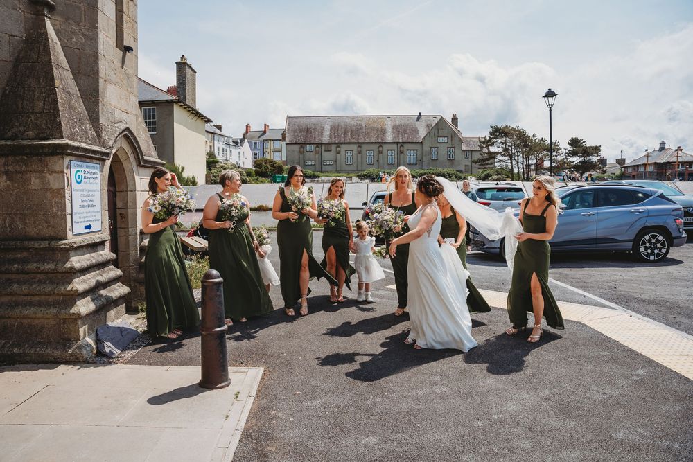 Wedding party taking casual outdoor photos on sunny day near stone building.
