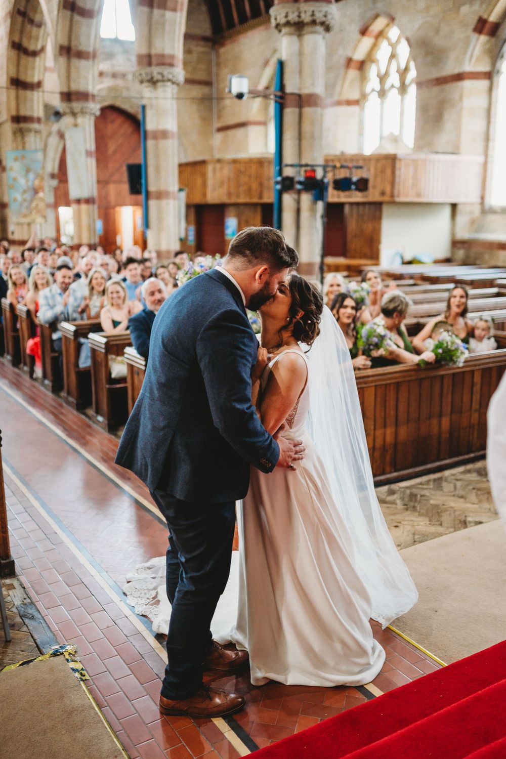 A romantic wedding moment captured on red carpet in a historic stone church with natural lighting.