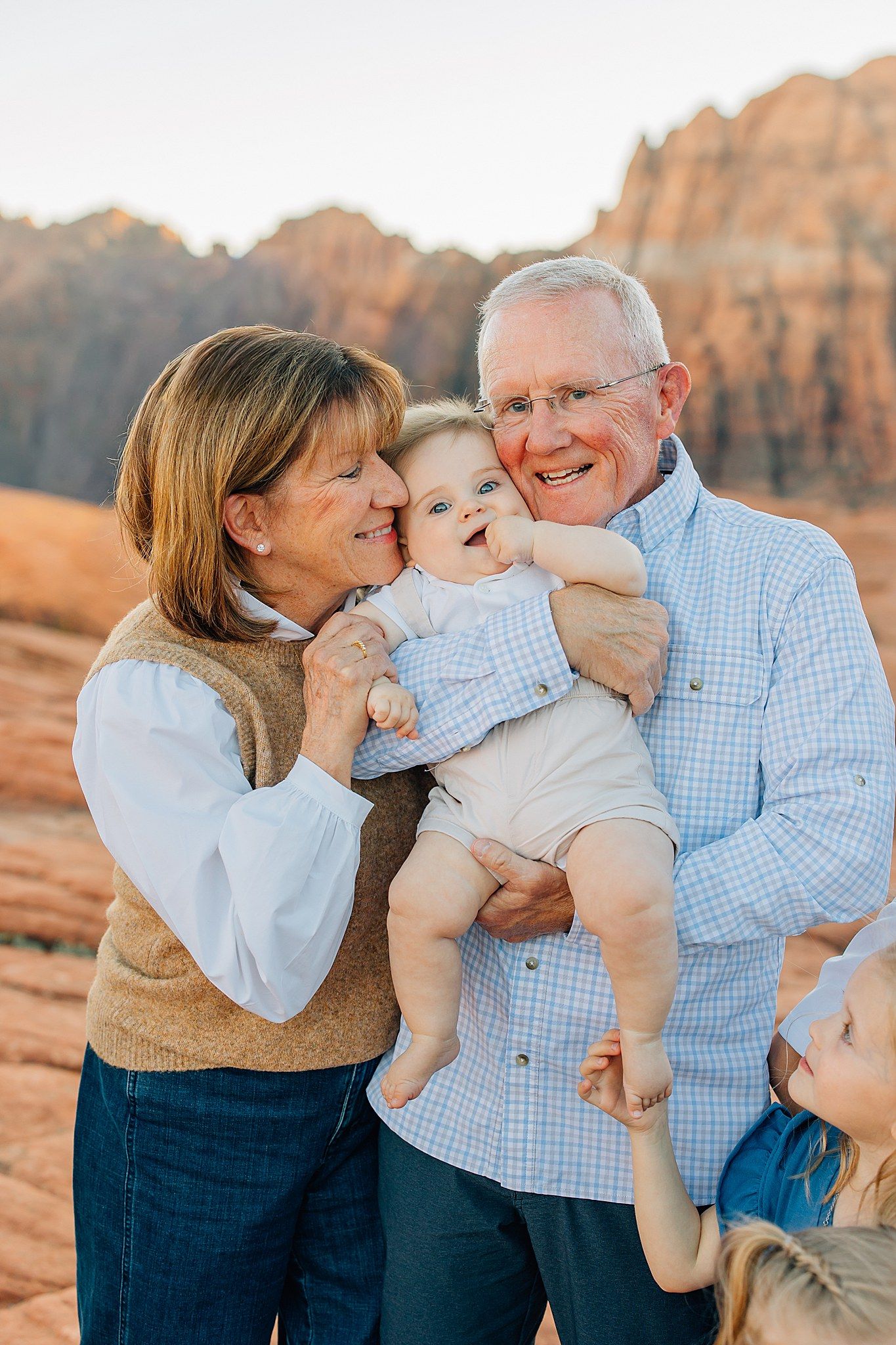 Family shares joyful moments together against backdrop of red rock formations at sunset.