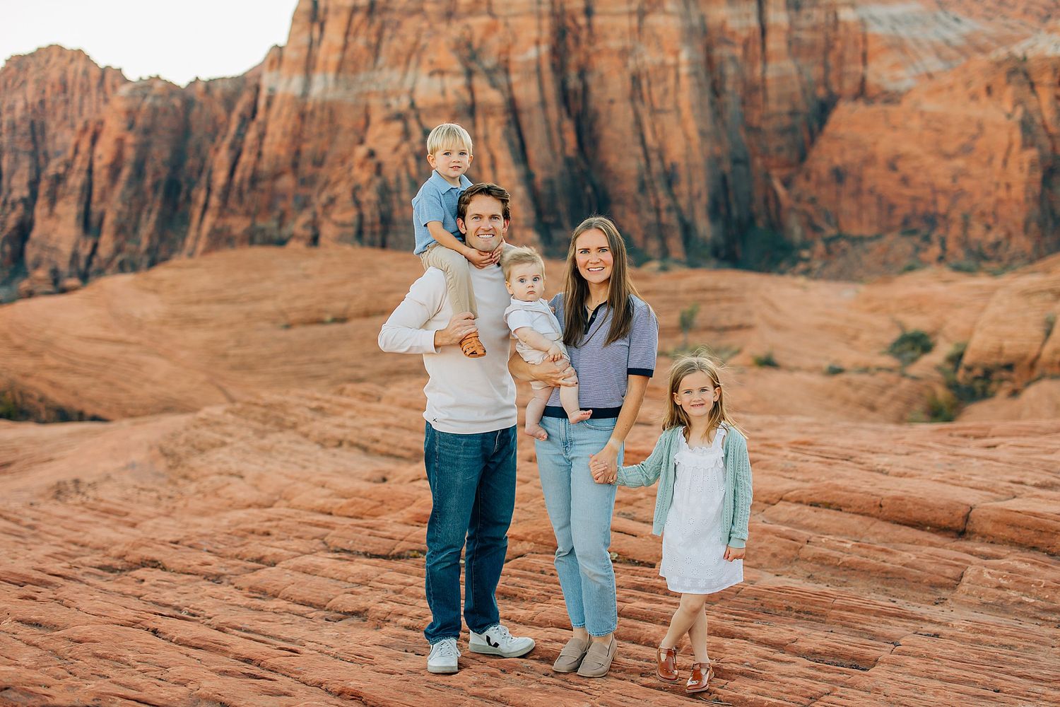 A family walks together along red rock formations in the desert during golden hour sunset.