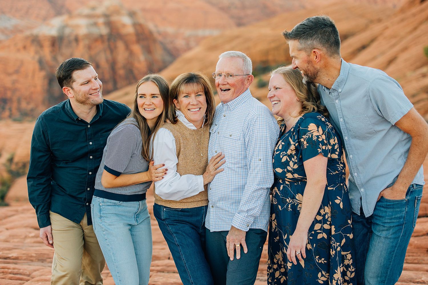 Family members embrace and laugh together while posing in front of towering red sandstone cliffs.