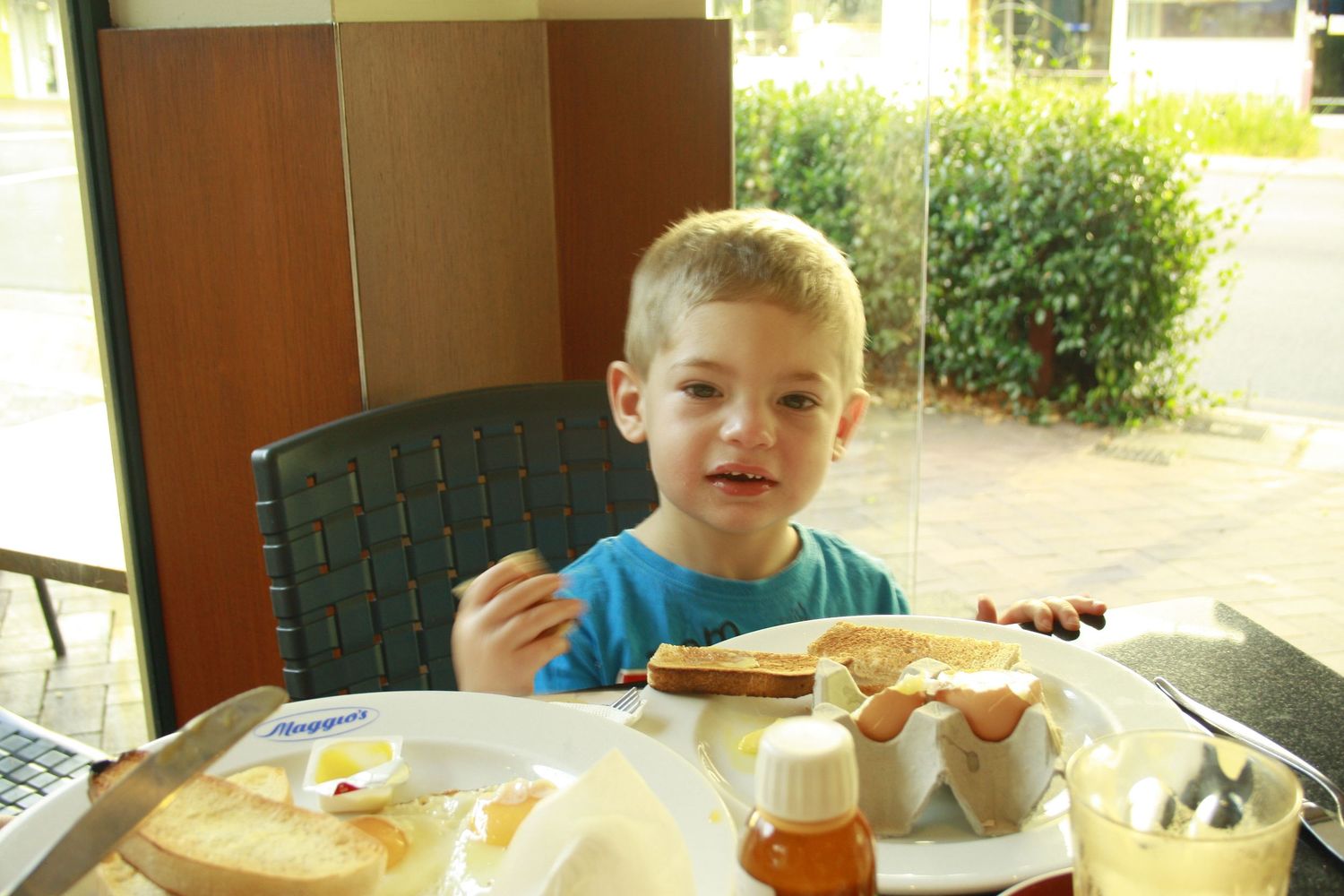 Children sit at a long table eating food and snacks during what appears to be a casual gathering or meal time.