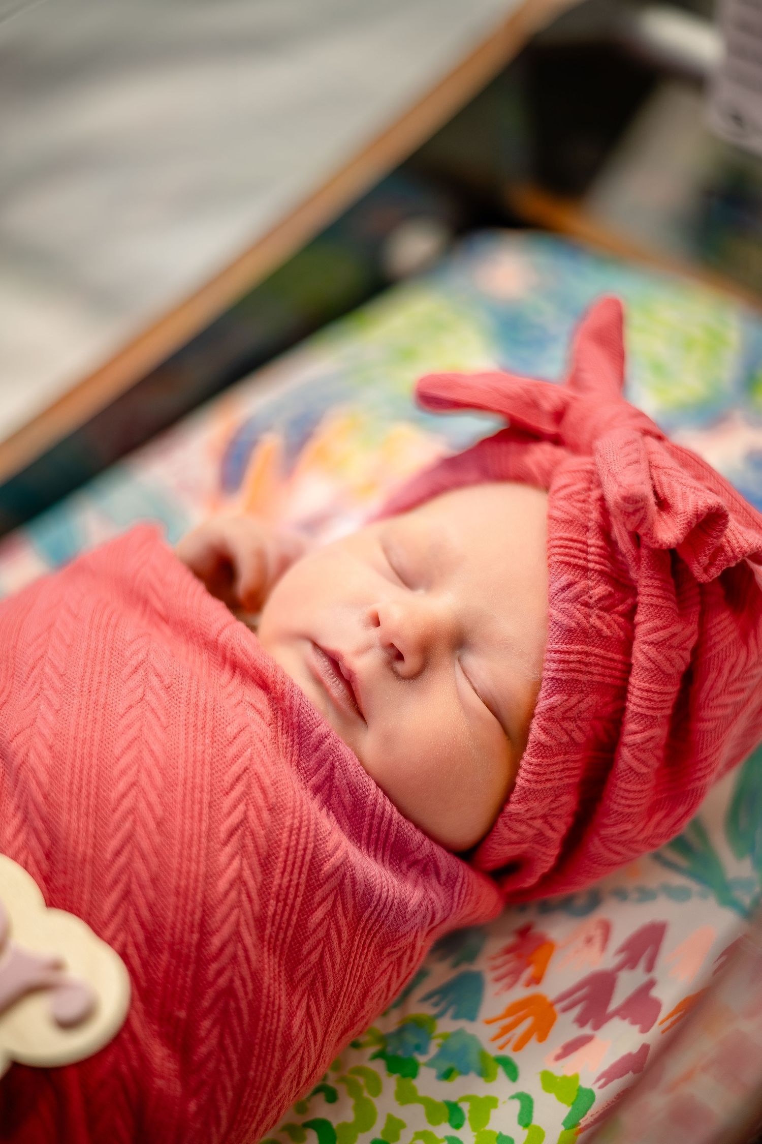 A sleeping baby wearing a red knit hat rests peacefully on a colorful floral patterned blanket.