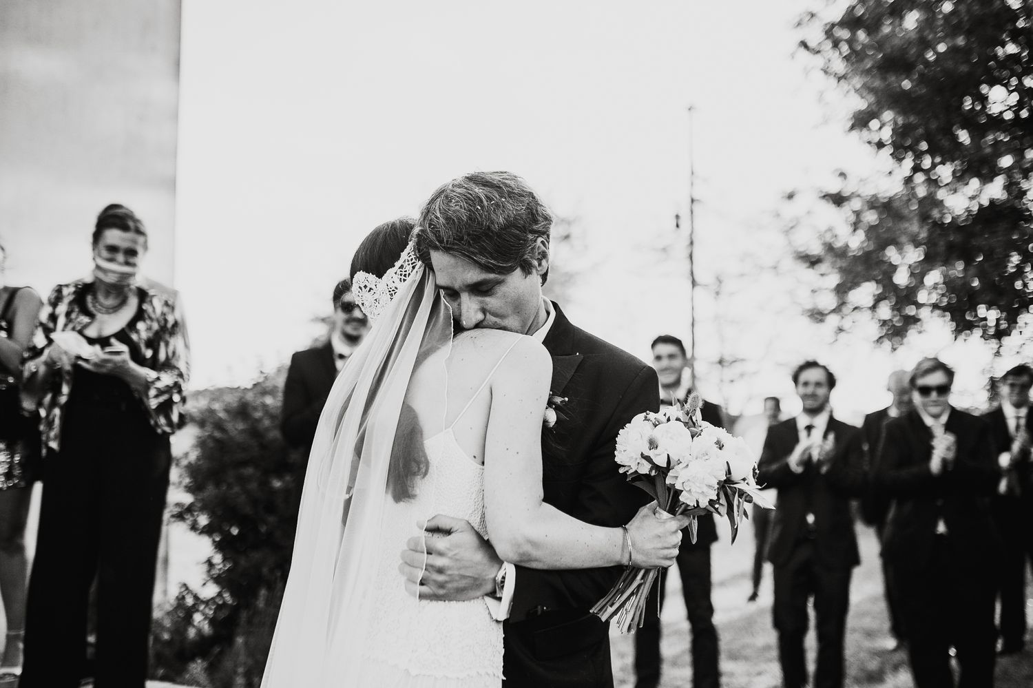 Wedding party gathered outdoors under trees in black and white photography.