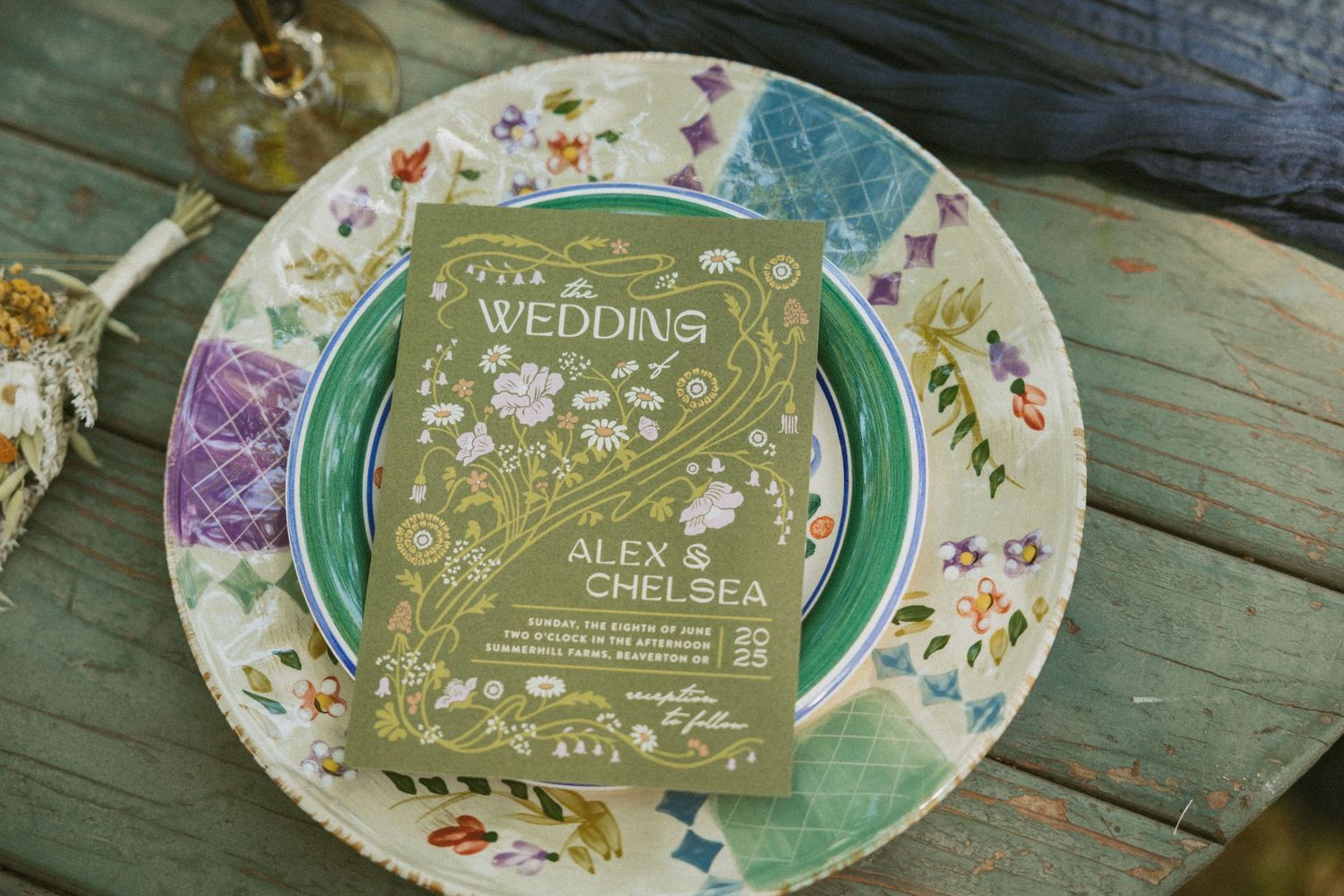 Vintage floral plates with green wedding invitations displayed on rustic wooden surface.
