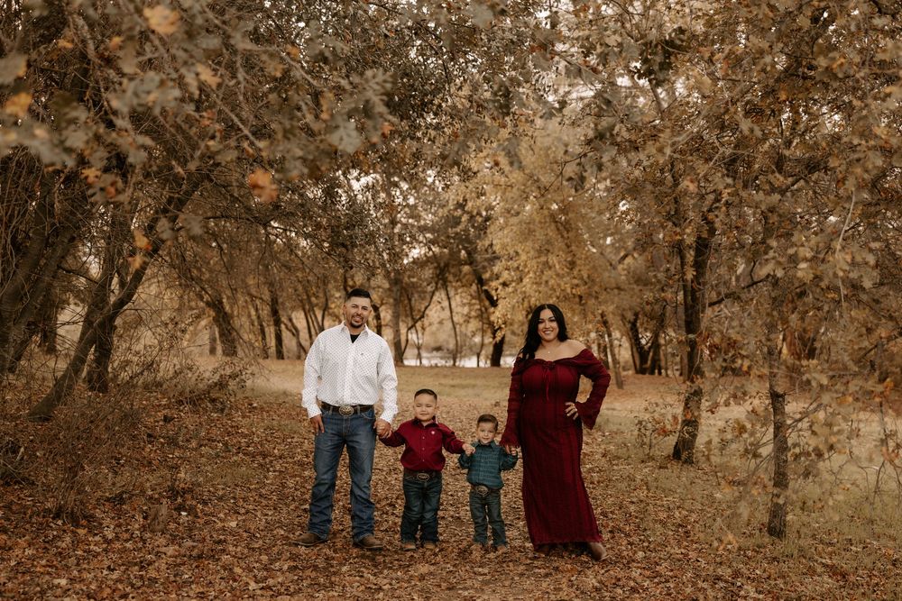 A family of four stands together in a wooded area with autumn trees and sepia-toned lighting.
