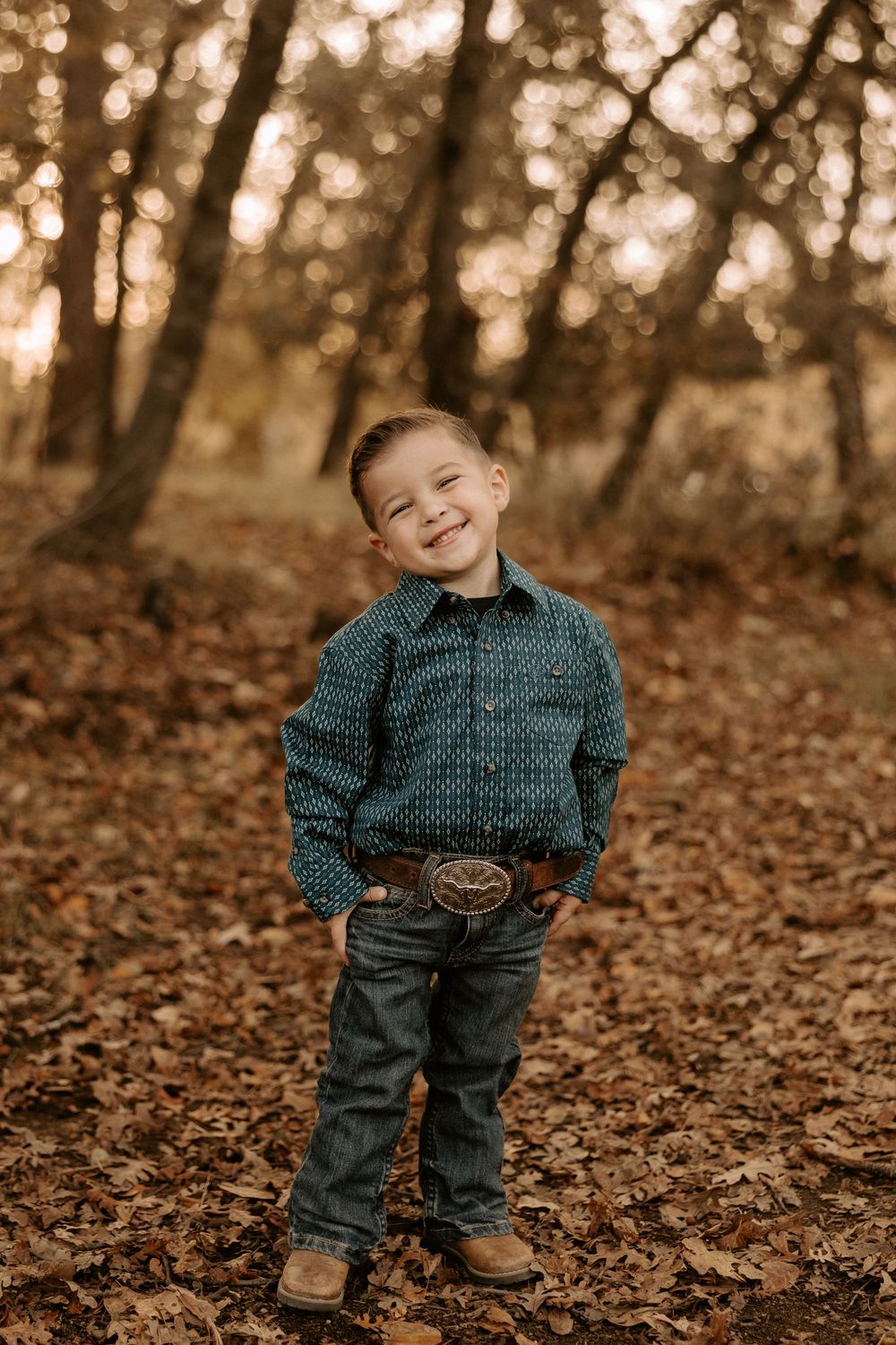 A child wearing a polka dot shirt and jeans stands in autumn leaves during a sepia-toned outdoor photo session.