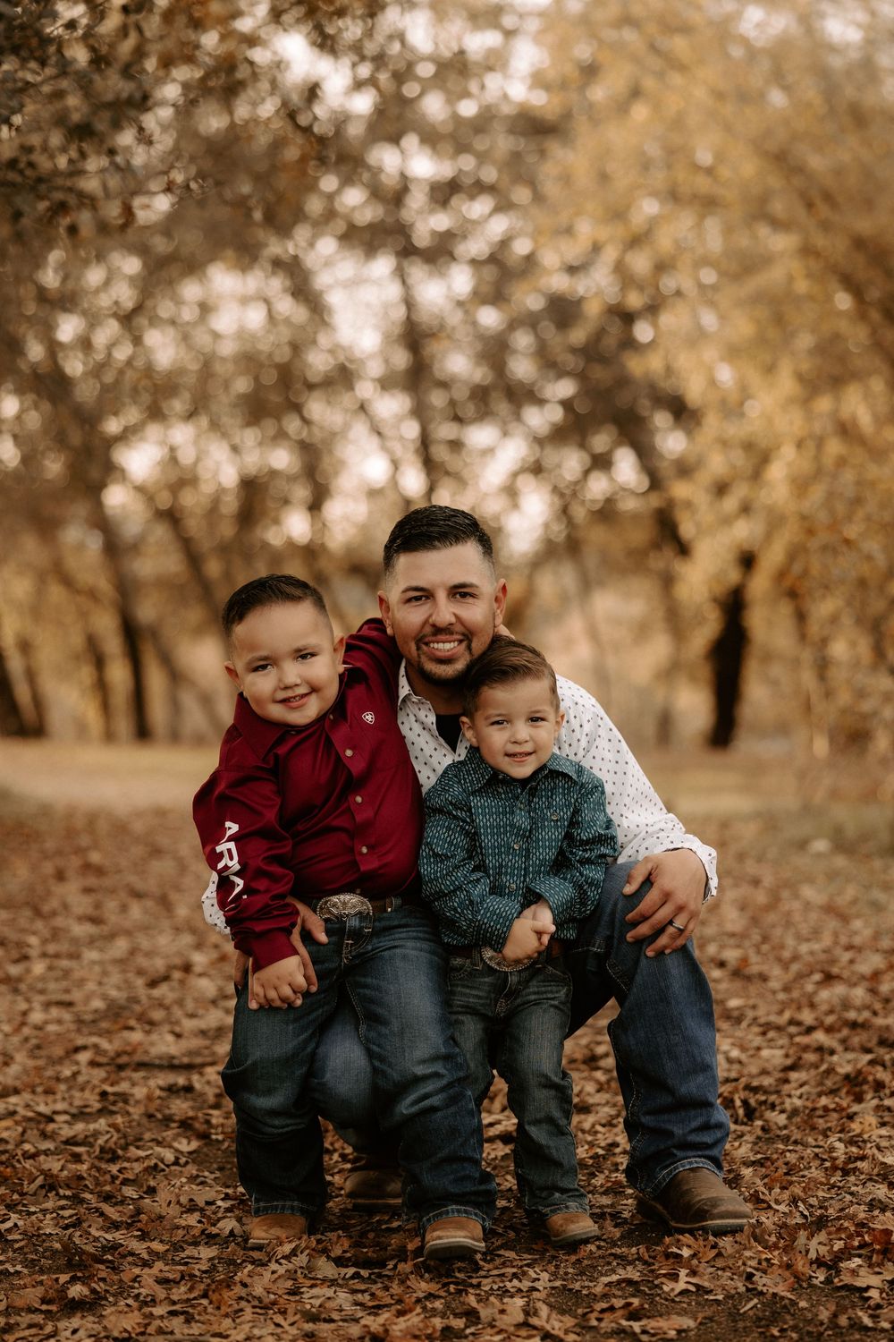 Family sitting together on fallen autumn leaves in a park during golden hour.