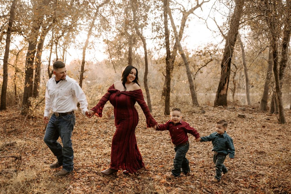 A family walks together through a sunlit autumn forest wearing coordinated burgundy and denim outfits.