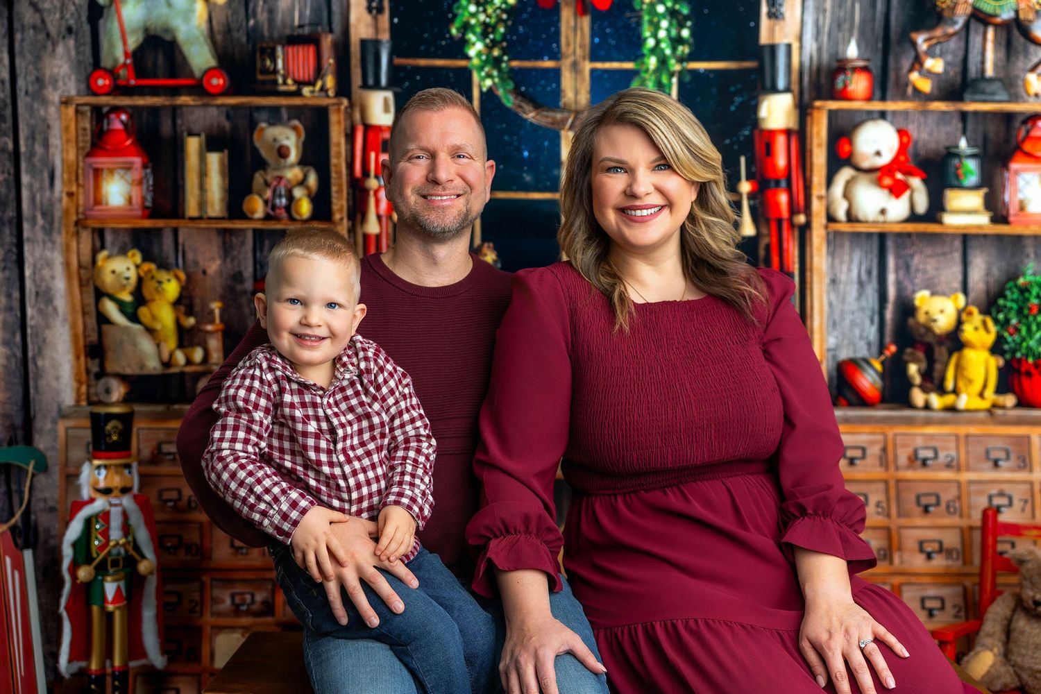 A family wearing coordinated burgundy and plaid outfits poses together in front of a festive holiday display.